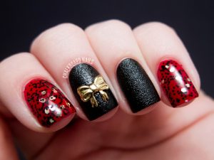 Black and red nail design with glitter accents and gold bow detail.
