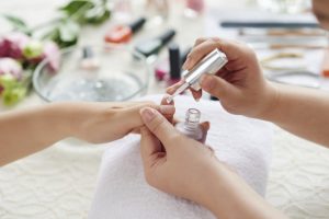 Pink nail polish being applied with a brush, in a salon setting, caring manicure process.