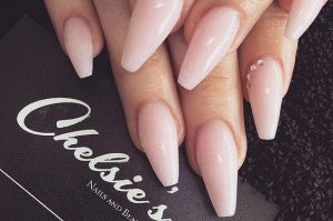 Long coffin-shaped nails with a nude glossy finish and pearl accents.