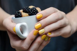 Yellow nails, glossy finish, short round shape, solid color with one accent nail with glitter.