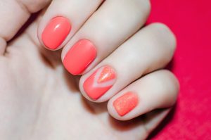 Short square nails with glossy finish, coral and glitter accents.