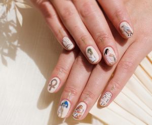 Short, oval nails with a glossy finish, featuring illustrated women and symbols.