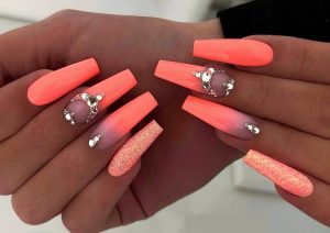 Long stiletto, almond shape, vibrant coral, matte and glitter finishes, rhinestone accents, glamorous and bold style.